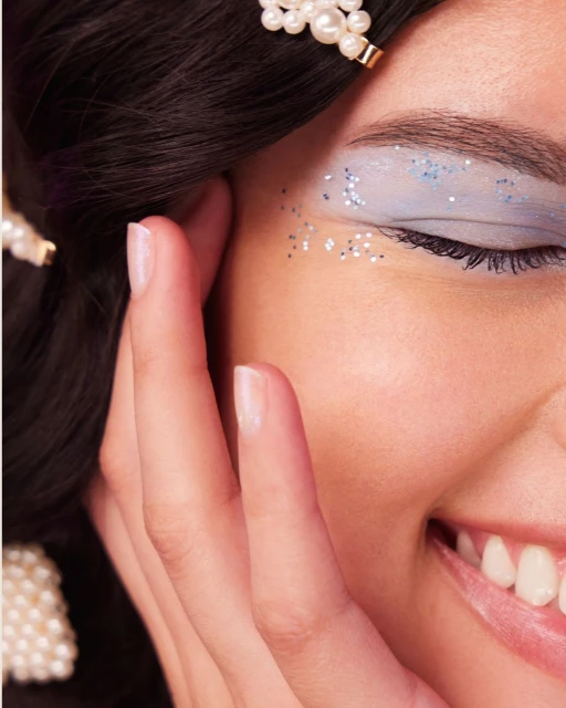 Close-up of a smiling woman with glitter eyeshadow and pearl hair accessories, focusing on beauty and fashionable makeup.