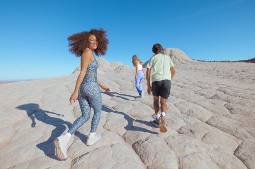 Three people walking up a textured rock formation under a clear blue sky, captured in bright natural daylight.