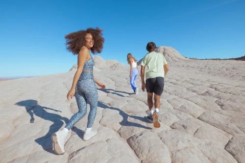 Three people walking up a textured rock formation under a clear blue sky, captured in bright natural daylight.