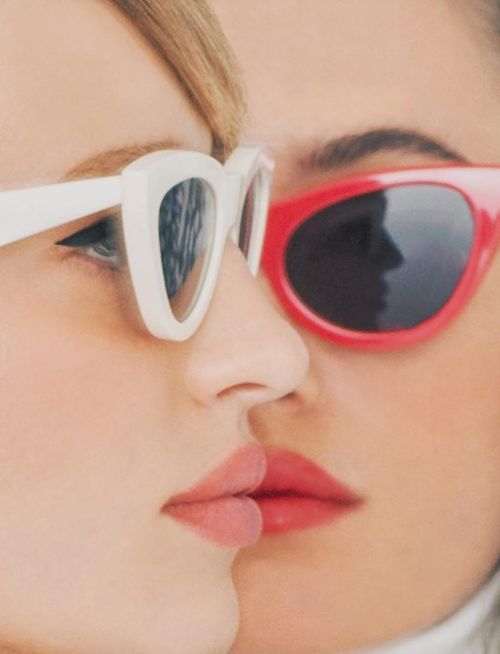 Close-up portrait of two women wearing white and red sunglasses with neutral lips.