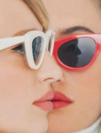 Close-up portrait of two women wearing white and red sunglasses with neutral lips.
