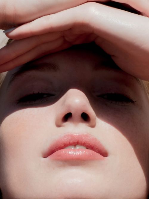 Close-up portrait of a woman with hands framing her forehead and natural sunlight casting shadows across her face.
