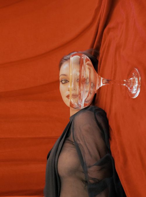 Surreal portrait of a woman's face partially distorted through a transparent glass, set against a bold orange fabric backdrop.
