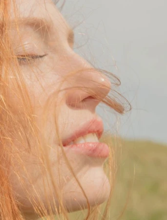 Close-up profile portrait of a woman with red hair blowing across her face outdoors