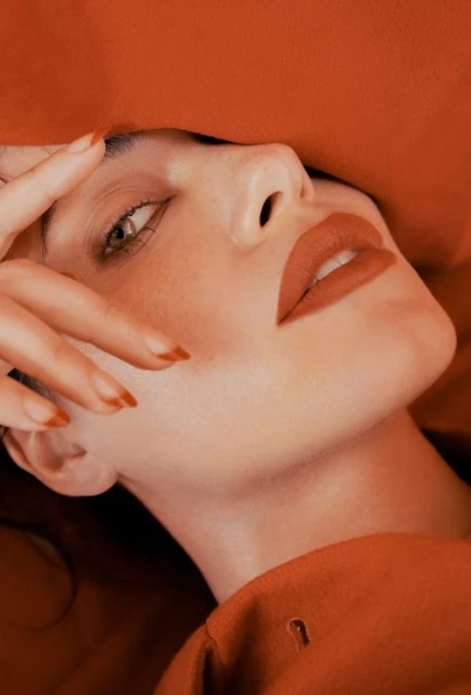 Close-up portrait of a woman with red lipstick and matching nail polish, posing against a monochromatic red backdrop with soft lighting.