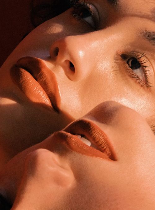 Close-up portrait of two faces overlapping with warm golden hour lighting and terracotta lipstick tones.