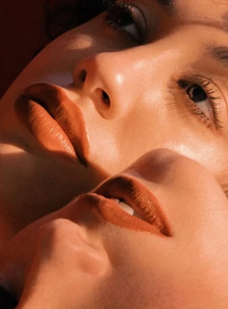 Close-up portrait of two faces overlapping with warm golden hour lighting and terracotta lipstick tones.