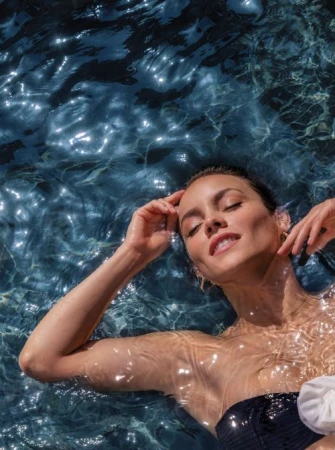 Woman with eyes closed floating in shimmering dark water wearing a dark swimsuit with white flower detail