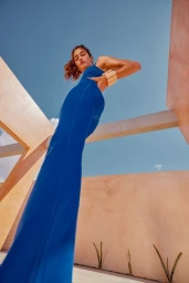 Low-angle shot of a woman in blue activewear against peachy architectural walls and a clear blue sky