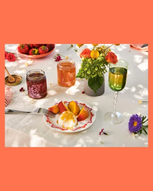 Still life photography of a dessert with peaches and cream, served on a decorative plate with flowers, fruit, and preserves.