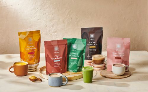 Assorted Clever Superlattes in colorful packaging with prepared mugs and cups displayed on a light-colored surface.