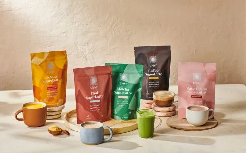 Assorted Clever Superlattes in colorful packaging with prepared mugs and cups displayed on a light-colored surface.
