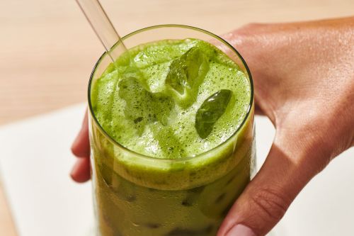 Close-up of a refreshing green matcha latte held by a hand, highlighting its vibrant color, foamy texture, and clear glass with a straw.