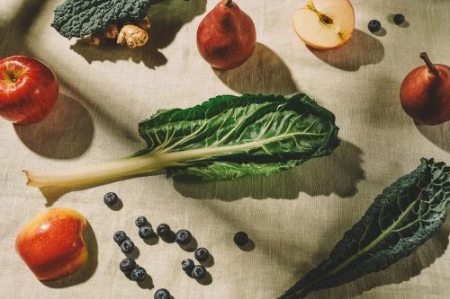 Overhead shot of an arrangement of apples, pears, blueberries, kale, ginger, and swiss chard on a neutral linen tablecloth.