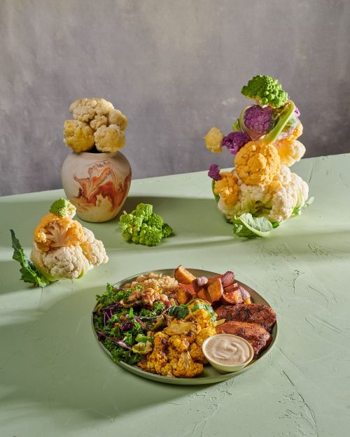 Colourful vegetarian buddha bowl with roasted vegetables and salad, with various cauliflower heads in the background, studio shot.