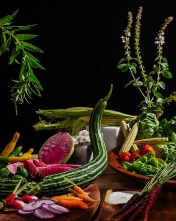 Still life food photography featuring an assortment of colorful, fresh vegetables including corn, carrots, radishes, and leafy greens.