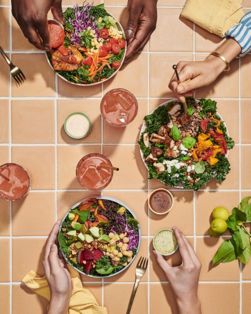 Overhead shot of healthy food bowls with salads and drinks, showcasing fresh ingredients and balanced meal options on a tiled surface.