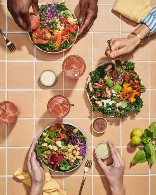 Overhead shot of healthy food bowls with salads and drinks, showcasing fresh ingredients and balanced meal options on a tiled surface.