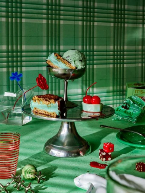 Still life of ice cream sandwiches and desserts on a table with a green tablecloth and checkered wallpaper background.