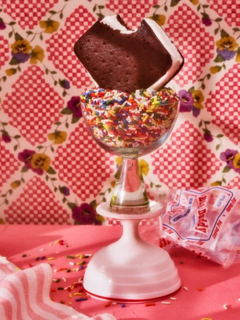 An ice cream sandwich, with a bite taken out, sits atop a glass filled with colorful sprinkles, creating a playful food photography.