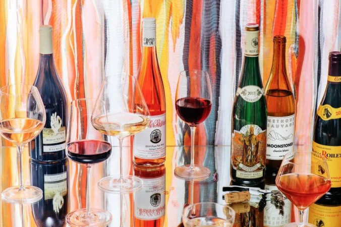 Multiple wine bottles and filled wine glasses arranged on a reflective surface against a colorful vertical striped backdrop
