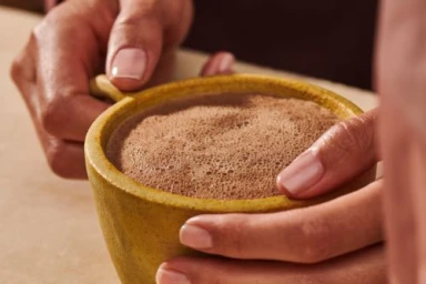 Close-up of hands holding a yellow ceramic mug filled with frothy hot chocolate, photographed by Julia Stotz.