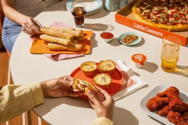 Overhead food photography of a table with Little Caesars pizza, breadsticks, cheesy puffs, and chicken wings.