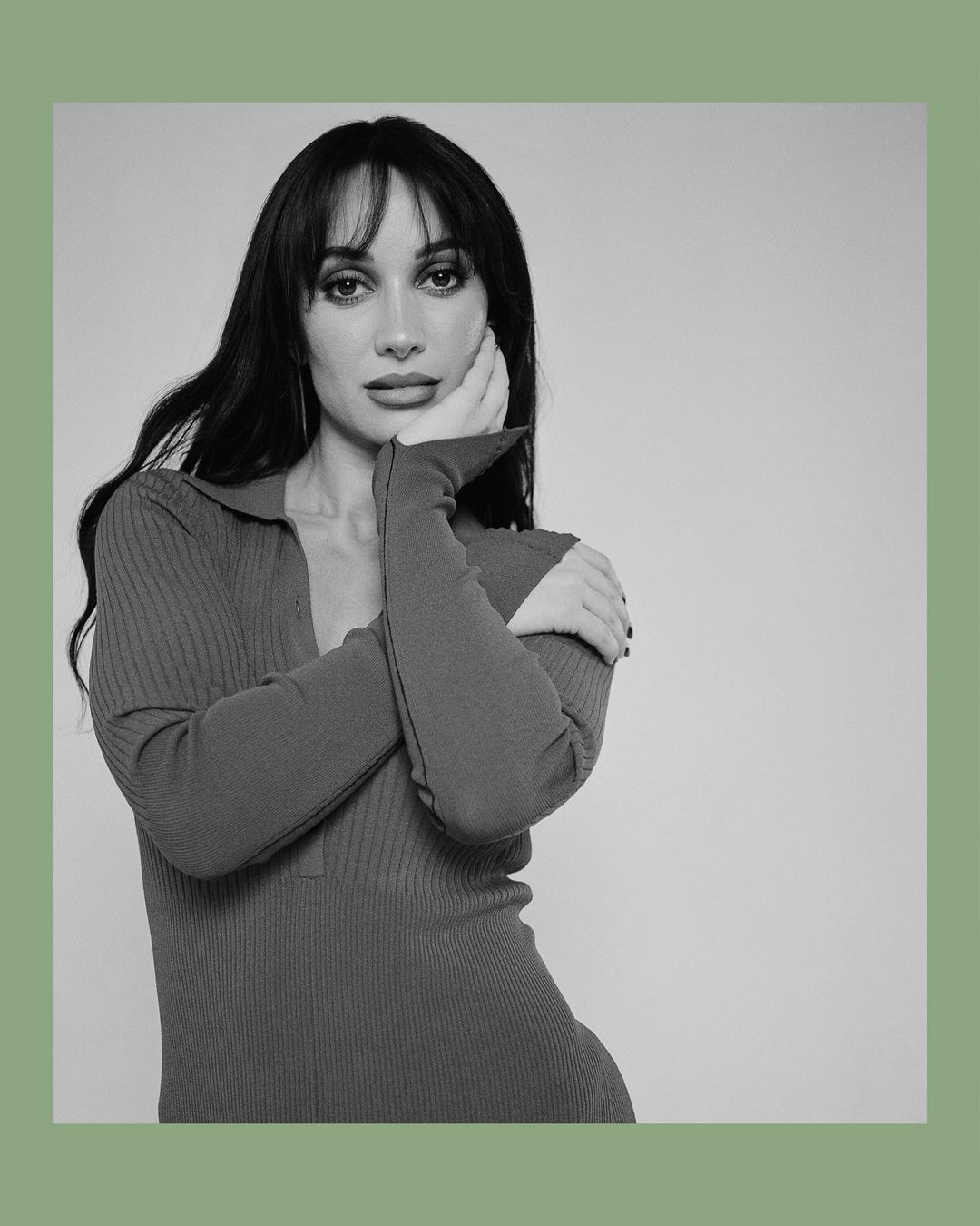 Portrait of a woman with dark hair and bangs posing with her hand to her cheek, wearing a ribbed polo dress