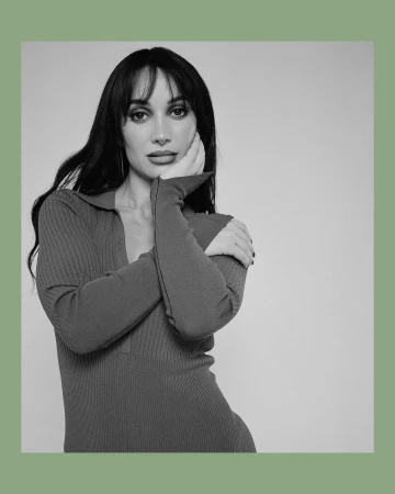 Portrait of a woman with dark hair and bangs posing with her hand to her cheek, wearing a ribbed polo dress