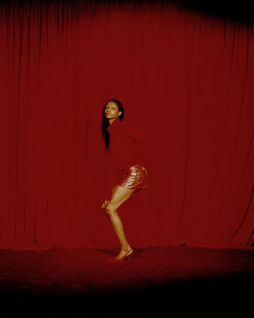Woman in red top and gold skirt poses in front of draped red fabric in a studio setting with low key lighting and medium shot.
