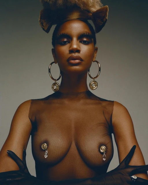 Close-up studio shot of a dark-skinned woman with creative makeup, gold hoop earrings, and hand jewelry against a gray background.