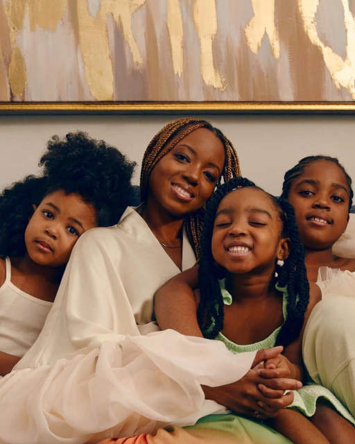 A heartwarming image shows a Black mother and her three daughters posing indoors in soft lighting, showcasing a loving family portrait.