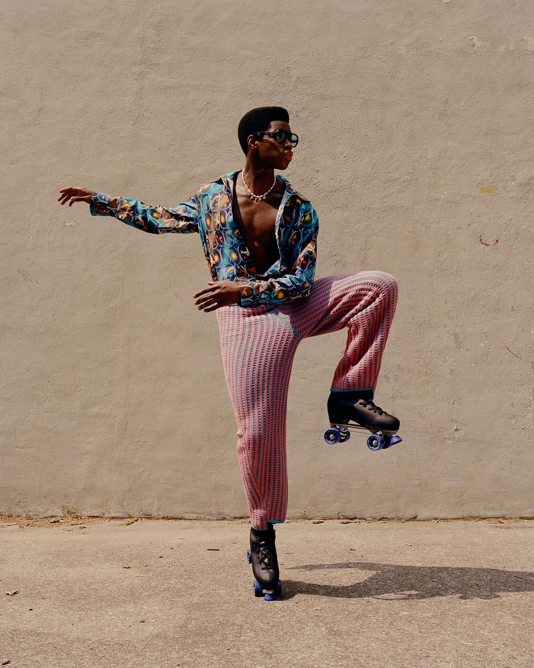 Adult male in patterned shirt and knitted pants roller skating outdoors. Bright sunlight and neutral background complement the fashion shot.