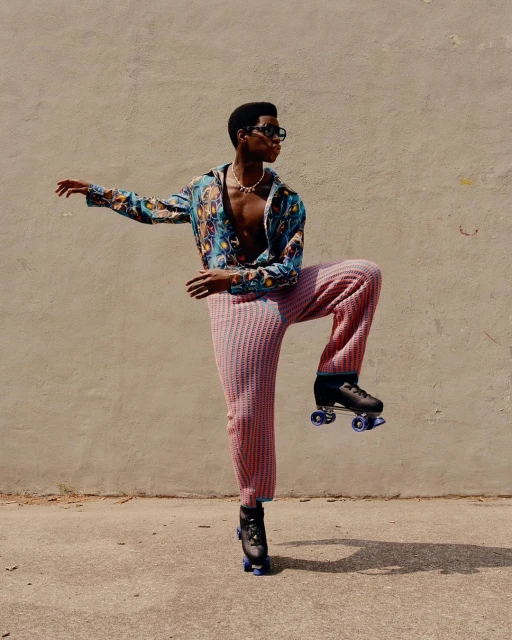 Adult male in patterned shirt and knitted pants roller skating outdoors. Bright sunlight and neutral background complement the fashion shot.