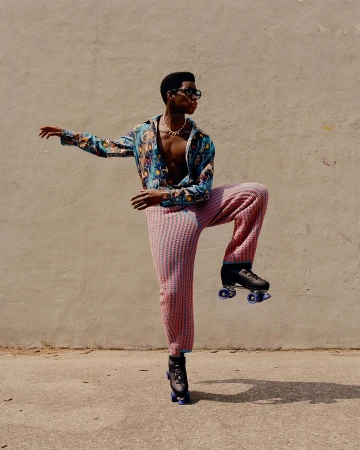 Adult male in patterned shirt and knitted pants roller skating outdoors. Bright sunlight and neutral background complement the fashion shot.
