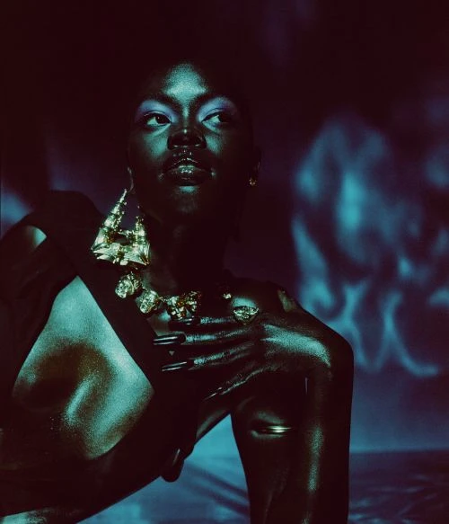 Glamorous portrait of a Black woman with statement jewelry in an indoor studio setting with moody lighting and a distinctive artistic aesthetic.