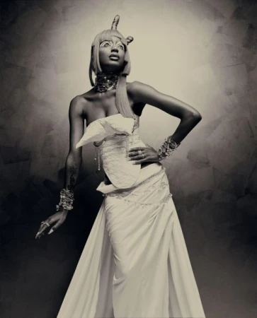 Elegant portrait of a woman in an elaborate white gown and headpiece, striking a pose against a textured, neutral-toned backdrop in the studio.