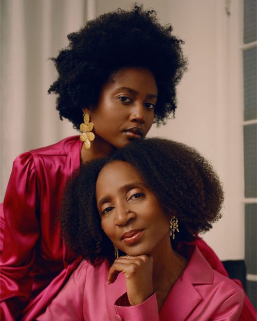 Two African American women in pink satin tops pose indoors. One woman is resting her head on the other's shoulder.