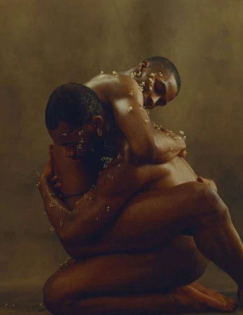Two Black men embracing closely, adorned with small white flowers against a warm textured background.