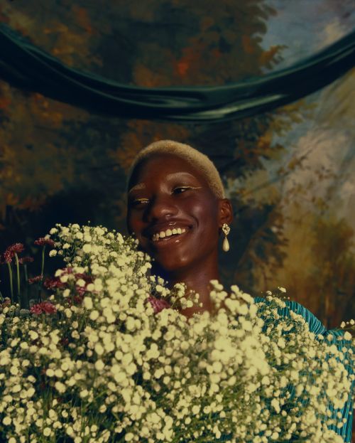 Smiling woman with flowers: close-up of a dark-skinned woman holding a bouquet of white flowers against a vintage, painted backdrop.
