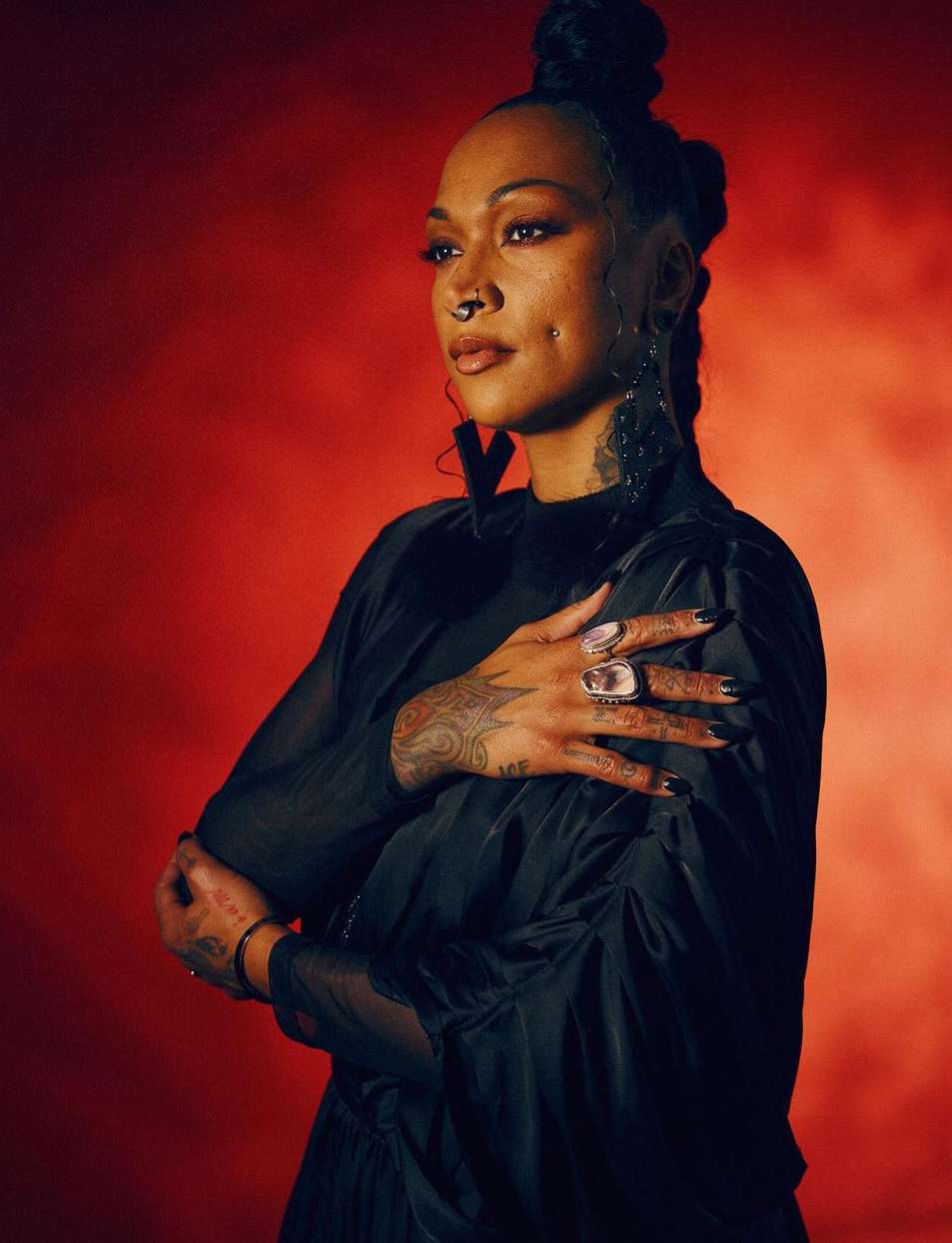 Portrait of a black woman wearing a black dress and statement rings against a red textured background shot by Kendall Bessent