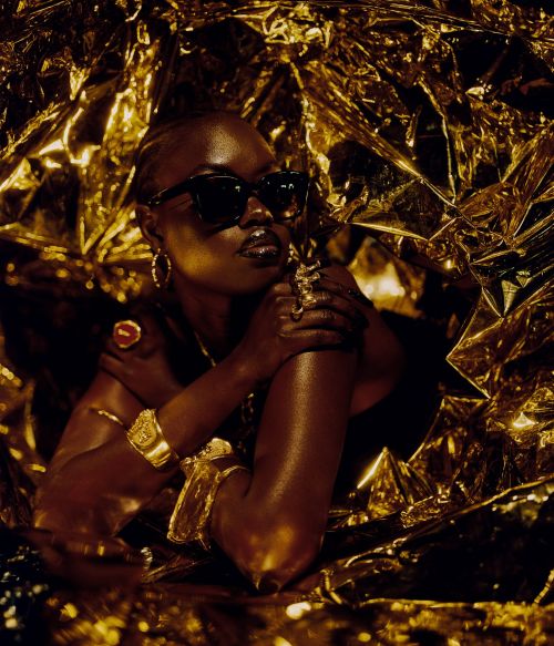 Portrait of an African woman wearing dark sunglasses, golden jewelry and wrapped in a golden reflective material, high fashion.