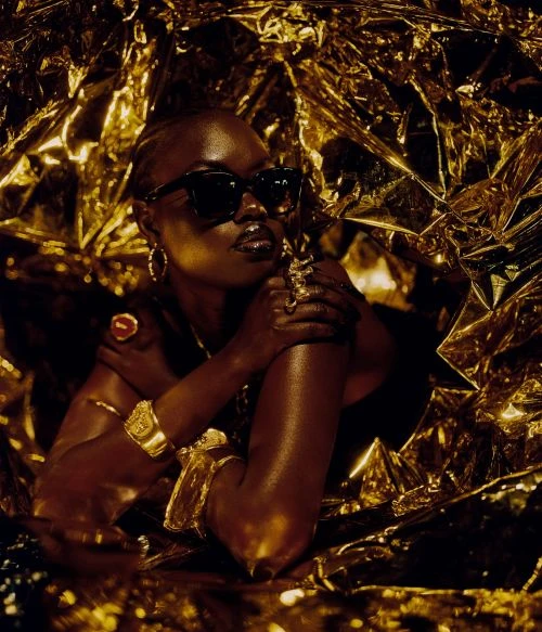 Portrait of an African woman wearing dark sunglasses, golden jewelry and wrapped in a golden reflective material, high fashion.