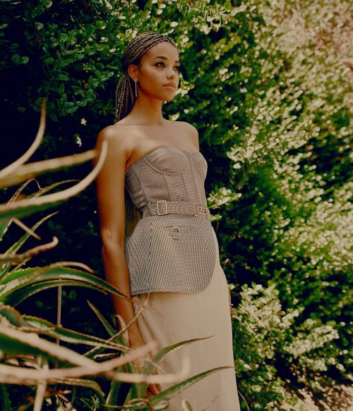 A stylish woman poses outdoors wearing a strapless bustier top and long skirt, complemented by green foliage and natural light.