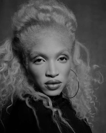 Monochrome portrait of a woman with voluminous light curly hair wearing hoop earrings and a dark top by Kendall Bessent