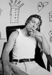 Monochrome portrait of a man wearing a white tank top seated in a chair against a background with hand-drawn sketches.