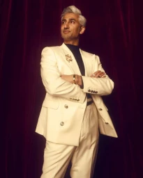 Tan France wearing an off-white double-breasted suit against dark red curtains, photographed by Kendall Bessent.