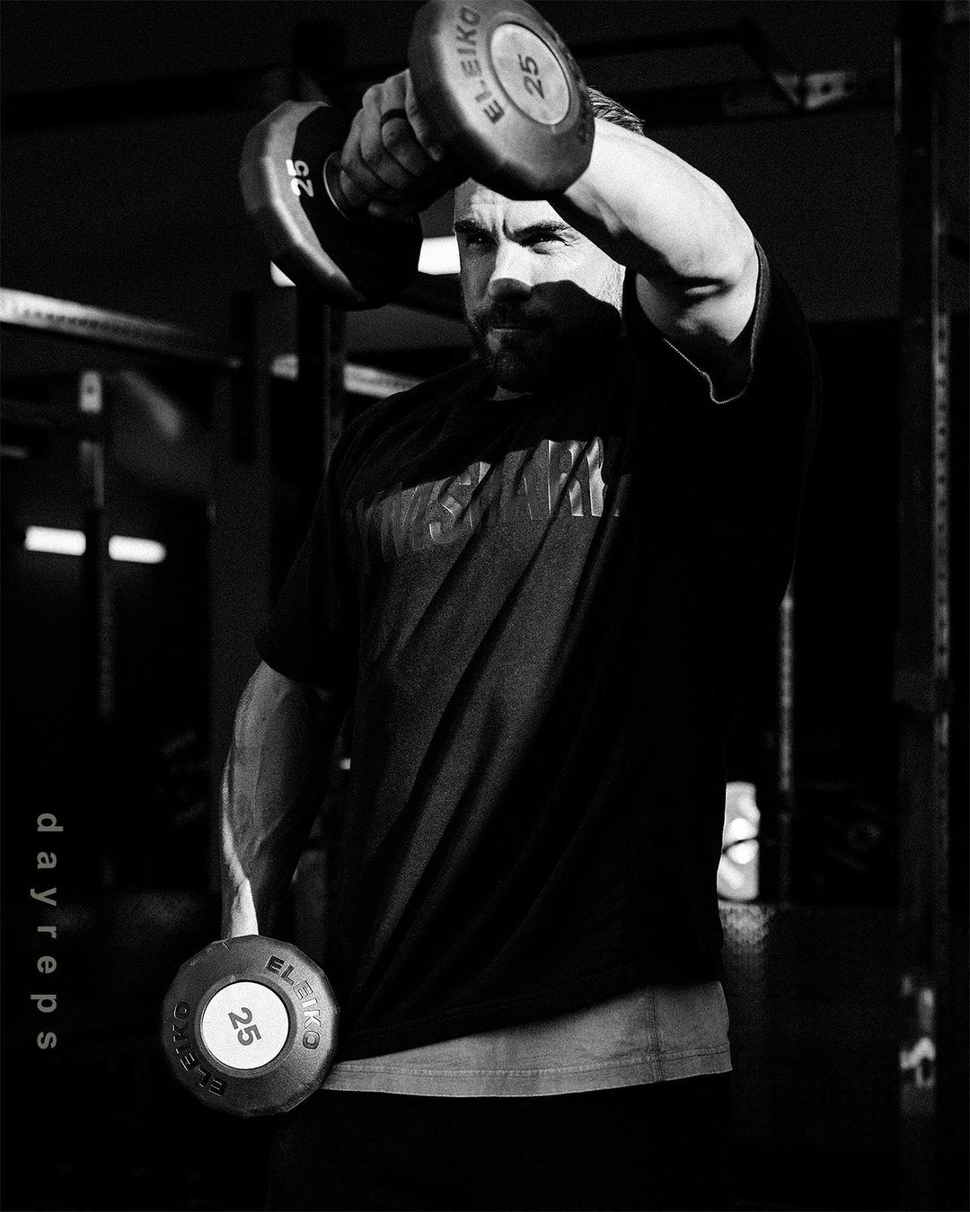 Black and white shot of an adult man lifting dumbbells in a fitness center, showcasing strength training in a gym environment.