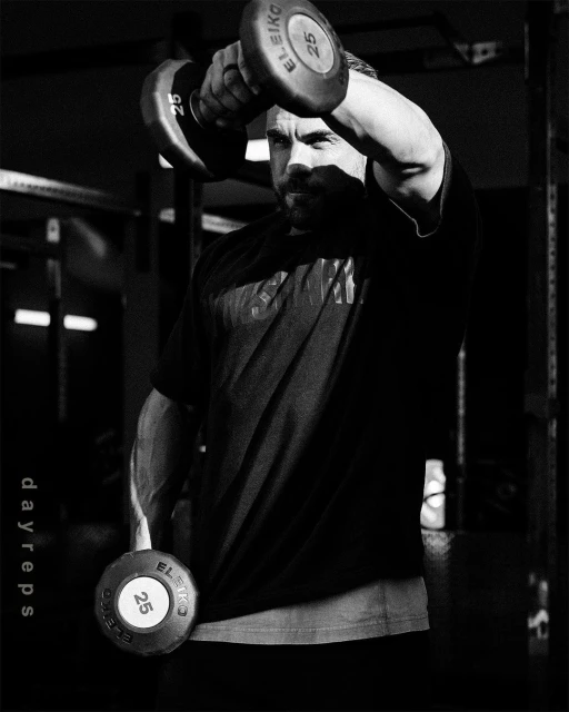 Black and white shot of an adult man lifting dumbbells in a fitness center, showcasing strength training in a gym environment.