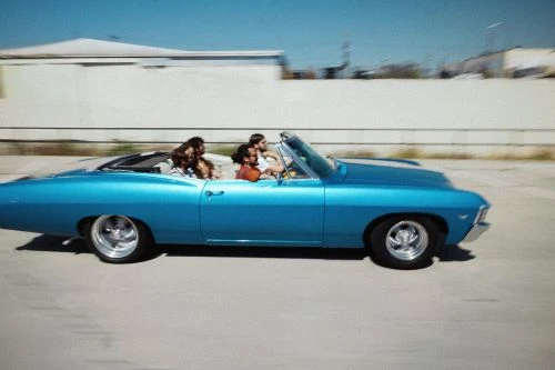 Classic turquoise convertible driving with a group of diverse young adult friends on a sunny day with motion blur.